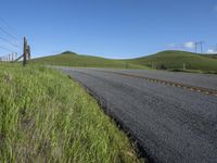 the grass grows in between the roadway and road area of a rural area under a bright blue sky