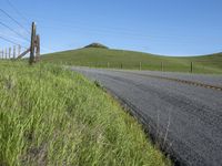 the grass grows in between the roadway and road area of a rural area under a bright blue sky