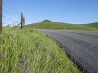 the grass grows in between the roadway and road area of a rural area under a bright blue sky