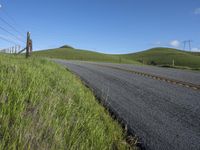 the grass grows in between the roadway and road area of a rural area under a bright blue sky