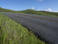 the grass grows in between the roadway and road area of a rural area under a bright blue sky