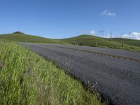 the grass grows in between the roadway and road area of a rural area under a bright blue sky