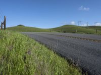 the grass grows in between the roadway and road area of a rural area under a bright blue sky