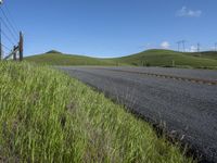 the grass grows in between the roadway and road area of a rural area under a bright blue sky