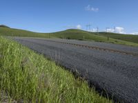 the grass grows in between the roadway and road area of a rural area under a bright blue sky