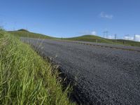 the grass grows in between the roadway and road area of a rural area under a bright blue sky