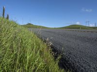 the grass grows in between the roadway and road area of a rural area under a bright blue sky