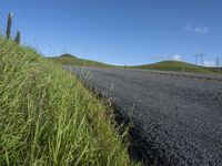 the grass grows in between the roadway and road area of a rural area under a bright blue sky