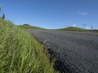 the grass grows in between the roadway and road area of a rural area under a bright blue sky