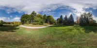 a panorama of some grass and some trees near a road and hill and a road