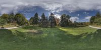 this is a photograph of a large grass park with trees in the background and clouds over the park