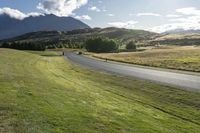 people riding motorcycles down a road through grass with mountains in the background / photographed from above