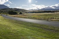 people riding motorcycles down a road through grass with mountains in the background / photographed from above