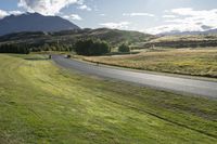 people riding motorcycles down a road through grass with mountains in the background / photographed from above