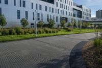 a city street surrounded by grass and tall buildings at the end of a street there is a paved pathway in front of the building