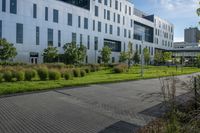 a city street surrounded by grass and tall buildings at the end of a street there is a paved pathway in front of the building