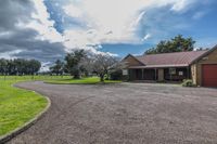 a gravel driveway leads to the front of a garage, which is next to a large grassy field