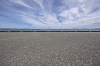 a gravel field on a sunny day with some clouds in the sky on the horizon