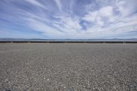 a gravel field on a sunny day with some clouds in the sky on the horizon