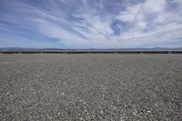 a gravel field on a sunny day with some clouds in the sky on the horizon