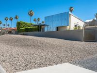 a gravel lot in front of a building with palm trees lining the sides and top