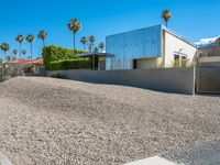 a gravel lot in front of a building with palm trees lining the sides and top