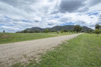 gravel path leading to grassy pasture with mountains in distance through clouds overhead in australia near cairns