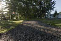 gravel pathway to an empty house by a wooded pond and forest on a sunny day