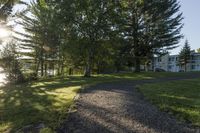 gravel pathway to an empty house by a wooded pond and forest on a sunny day