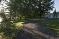 gravel pathway to an empty house by a wooded pond and forest on a sunny day