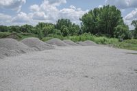 a pile of gravel on the ground with trees in the background and clouds above it