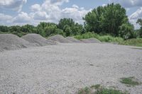 a pile of gravel on the ground with trees in the background and clouds above it