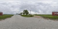 an empty gravel road lined with parked buildings in a farm town, on a cloudy day