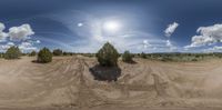 this is a 360 - image of dirt road in the desert with a few clouds in the sky