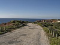 gravel road with grassy fields along side of ocean and rocky cliff cliffs on either side