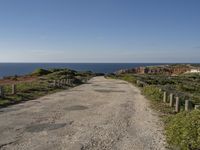 gravel road with grassy fields along side of ocean and rocky cliff cliffs on either side