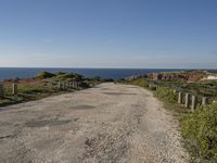 gravel road with grassy fields along side of ocean and rocky cliff cliffs on either side