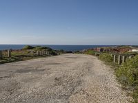 gravel road with grassy fields along side of ocean and rocky cliff cliffs on either side