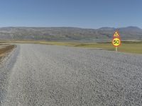 a road with gravel and a speed limit sign that says 65 degrees down on it