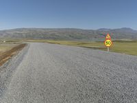 a road with gravel and a speed limit sign that says 65 degrees down on it