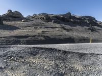 a car drives down a gravel road by rocks and boulders on a mountain side with a bright blue sky