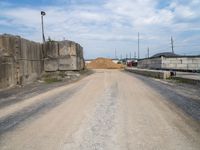 a gravel road with a large pile of dirt in the background and power lines going over the street