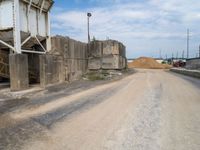 a gravel road with a large pile of dirt in the background and power lines going over the street