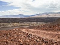 gravel road winding through barren terrain into the distance of mountain range and hills in the background