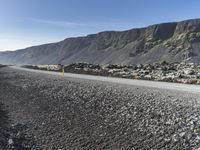 the road has gravel and rocks by it and mountains in the background of the scene