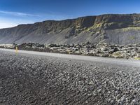 the road has gravel and rocks by it and mountains in the background of the scene