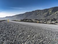 the road has gravel and rocks by it and mountains in the background of the scene