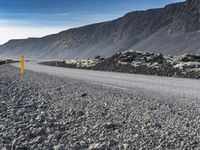 the road has gravel and rocks by it and mountains in the background of the scene