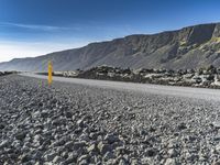 the road has gravel and rocks by it and mountains in the background of the scene