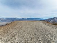 a large gravel road with mountains in the background and a dog walking across it to the top